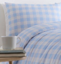 Blue and white checkered bedding with a cup on a table in the foreground.