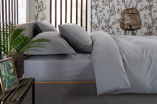 Silver grey bedding set on a bed with a decorative plant and side table in a bedroom setting.