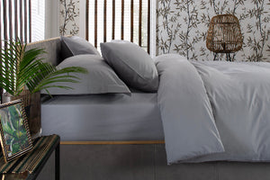 Silver grey bedding set on a bed with a decorative plant and side table in a bedroom setting.
