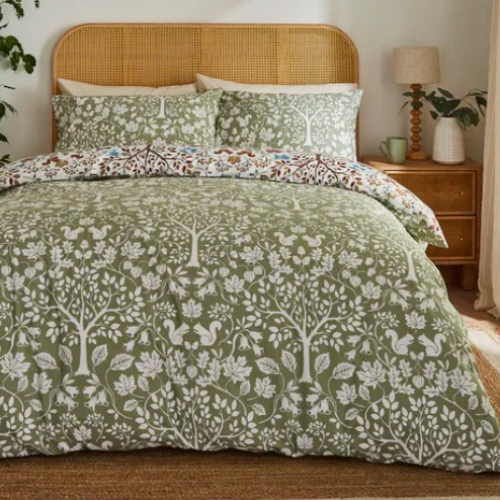 Bed with green floral and tree patterned bedding in a bedroom setting.