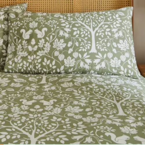 Green and white floral and animal patterned bedding set on a bed with a wooden headboard.